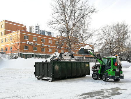 Moscow. Russia. January 15, 2021. Small front-end loaders clear snow from the street and load into a bunker for removal. Utilities work after heavy snowfall.のeditorial素材