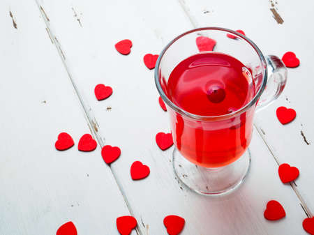 Selective focus on cranberries in a fresh drink in a glass cup on a white wooden background. Many small red hearts as a symbol of Valentines Day. Close-up. Copy space.の写真素材