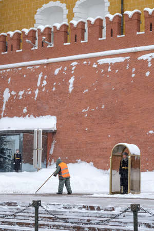 Moscow. Russia. February 12, 2021. A soldier on guard at the Kremlin wall at the tomb of the unknown soldier on a winter day. A utility worker removes snow after heavy snowfall.のeditorial素材