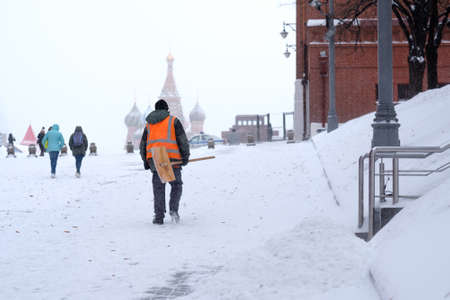 Moscow. Russia. February 12, 2021. A male utility worker in Red Square shovels snow after a heavy snowfall. Against a blurred background, the Orthodox Church of St. Basil the Blessed and Mausoleum.のeditorial素材
