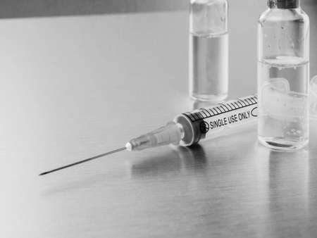 Syringes and ampoules on a polished metal background. Coronavirus vaccination and immunization concept. Selective focus. Black and white monochrome image. Copy space.の写真素材