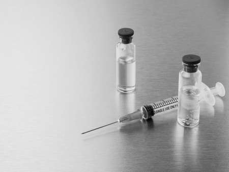 Syringes and ampoules on a polished metal background. Coronavirus vaccination and immunization concept. Selective focus. Black and white monochrome image. Copy space.の写真素材