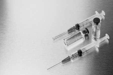 Syringes and ampoules on a polished metal background. Coronavirus vaccination and immunization concept. Selective focus. Black and white monochrome image. Copy space.の写真素材