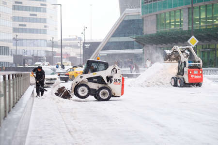 Moscow. Russia. February 12, 2021. Two small excavators - loaders with buckets remove snow from a...