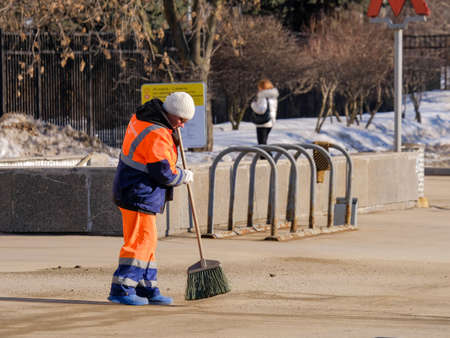 Moscow. Russia. March 24, 2021. A woman janitor in orange uniform sweeps the pavement with a broom...