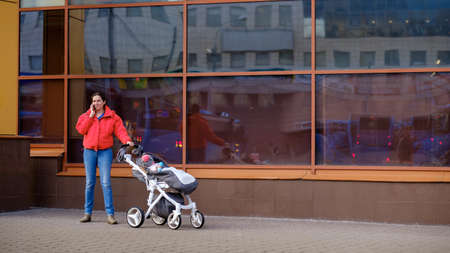 Moscow. Russia. March 26, 2021. A young woman in a red jacket with a stroller is talking on the...