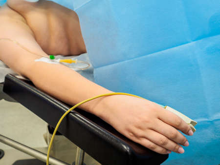 The hand of a woman patient lying on the operating table. On the finger is a pulse oximeter sensor, and in the hand there is an intravenous catheter for a dropper containing anesthesia.の写真素材