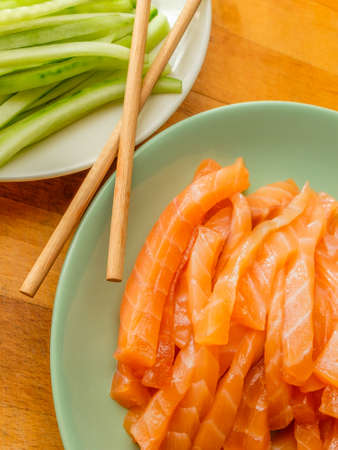 Selective focus on salmon and fresh cucumber slices on plates and bamboo chopsticks. Flat lay. Appetizing vibrant ingredients from Asian cuisine.の写真素材