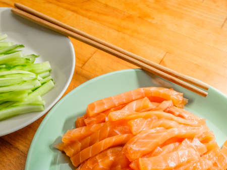 Selective focus on salmon and fresh cucumber slices on plates and bamboo chopsticks. Flat lay. Appetizing vibrant ingredients from Asian cuisine.の写真素材
