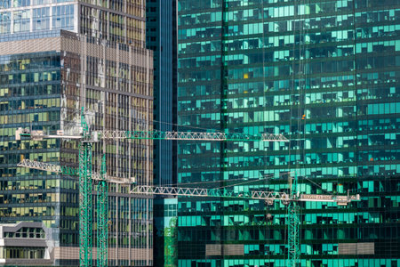 Moscow. Russia. April 18, 2021. Construction cranes against the backdrop of glass facades of huge skyscrapers on a sunny day. The concept of the modern construction industry in the metropolis.のeditorial素材