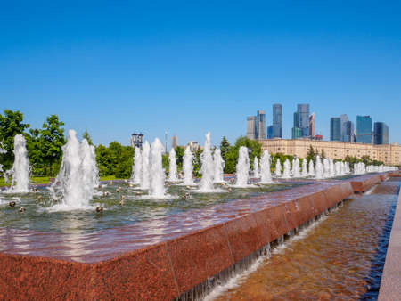 Jets of fountains on a sunny day against the backdrop of modern skyscrapers and a cloudless blue sky. Recreation area in Victory Park on Poklonnaya Hill in summer.の写真素材