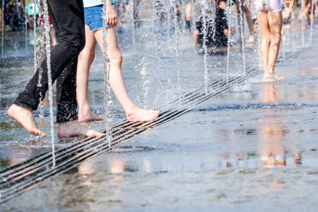 Selective focus on bare feet of woman in spray of water on a sunny summer day. People in the city escape from the heat by bathing in fountains.の写真素材
