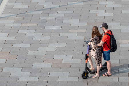 Moscow. Russia. June 26, 2021. A couple in love, a girl and a guy together stand on the same electric scooter on the pavement on a summer day. Modern electric eco-friendly urban transport. Copy spaceのeditorial素材
