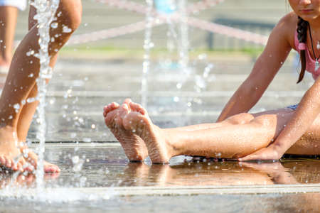 Selective focus on the bare feet of a girl refreshing herself on the floor of a fountain in splashes...