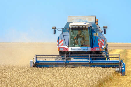 Krasnodar region. Russia. July 12, 2021. A modern blue agricultural harvester mows ripe yellow dried...