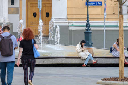 Moscow. Russia. 01 August 2021 An attractive young girl sits at the city fountain on a summer day....