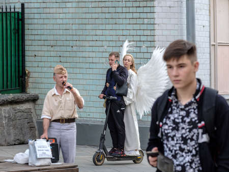 Moscow. Russia. August 1, 2021. A young girl with white angel wings and a young man ride together on an electric scooter along a city street during the day.のeditorial素材