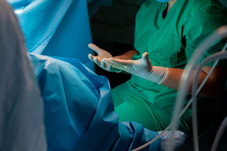 Surgeons hands in sterile latex gloves. A surgeon in a green uniform pulls forward the spread...