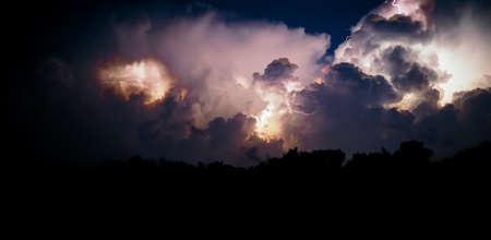Electrical discharges of lightning in the night sky. Thunderclouds and lightning flashes during a thunderstorm at night. Panoramic photo.の写真素材