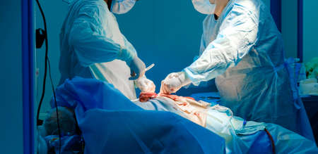 Two surgeons in blue uniforms operate on a patient on an operating table. Selective focus. Surgical instruments in the hands of doctors during a surgical operation.の写真素材