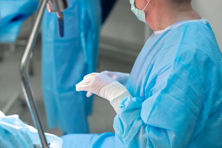 Selective focus on the hands of the surgeon in white sterile gloves in the operating room. A...