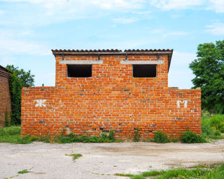 Old public toilet made of red brick on the street on a summer day. On the wall there are Russian letters M and Zh.の写真素材