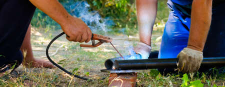 Hands of male workers welding metal pipes by electric arc welding on a summer sunny day. Widescreen image. Banner.の写真素材