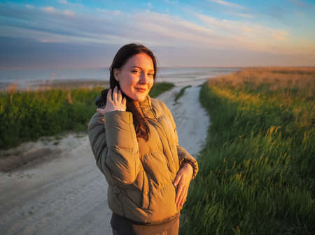 Portrait of a young woman by the sea at sunset. Young girl on the beach during sunset on a cold evening.の写真素材