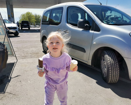 Moscow. Russia. May 8, 2022. A little blonde-haired child girl holds two ice creams in her hands on a sunny day. Happy child with ice cream.のeditorial素材