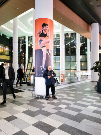 Moscow. Russia. February 3, 2022. A man in a shopping center uses a smartphone in front of an advertisement for sports equipment.のeditorial素材
