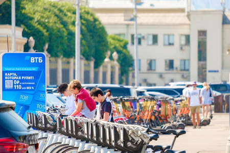Moscow. Russia. June 9, 2022. A young guy in the parking lot chooses a bike for rent. Selective focus. Public environmentally friendly transport on a summer sunny day on a street in Moscow.のeditorial素材