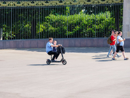 Moscow. Russia. June 9, 2022. Father and son ride together on the same electric scooter along the city street on a summer sunny day. Friendly family concept.のeditorial素材