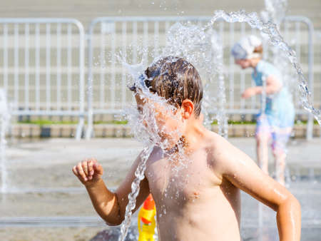 The jet of water from the fountain splashes in the boys face. The boy bathes and has fun between the...