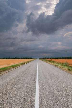 Asphalt road going into the distance against a dark stormy sky.の写真素材