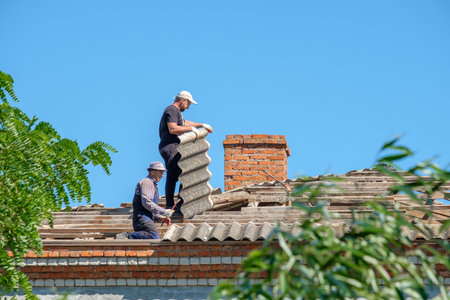 Krasnodar region. Russia. July 15, 2022. Workers on the roof of a building are dismantling old sheets of asbestos slate. Roofers are repairing the roof.のeditorial素材