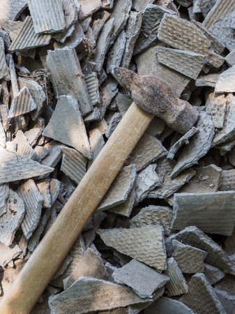 An old hammer lies on pieces of old broken slate. A hammer against the background of randomly scattered pieces of broken asbestos.の写真素材