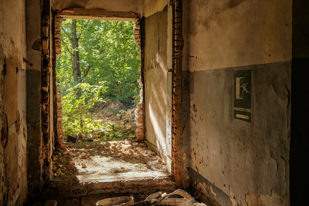 Empty doorway in an abandoned brick house with sunlight on dilapidated walls. The concept of poverty or war damage. Emergency exit sign on the wall.の写真素材