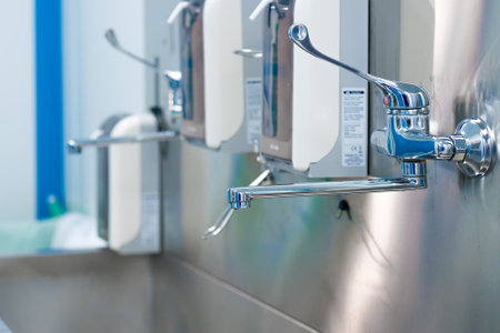 Selective focus on a shiny faucet of a sterile steel washbasin in a modern operating room. Hand washing room in a hospital.の写真素材
