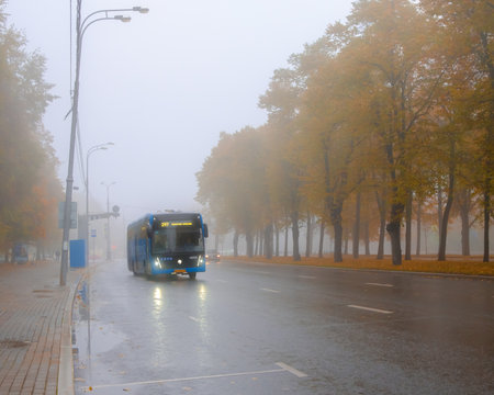 Moscow. Russia. October 1, 2022. Blue urban electric bus in dense fog on an autumn day. An electric bus drives down the street past trees with falling leaves.のeditorial素材