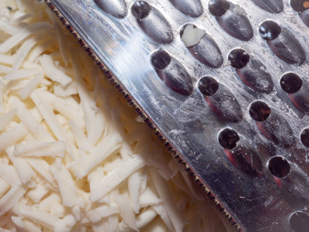 Metal kitchen grater on the background of freshly grated mozzarella cheese close-up. Selective focus.の写真素材