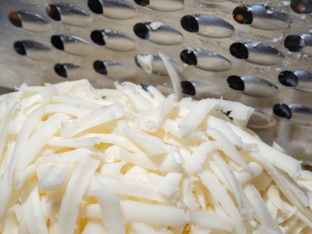 Freshly grated mozzarella cheese close-up on the background of a metal kitchen grater. Selective...