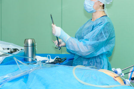 The doctor holds a sterile surgical instrument near the table in the operating room.の写真素材