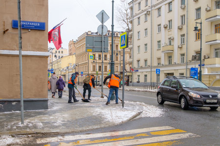 Moscow. Russia. February 25, 2023. Workers in orange vests shovel snow off the sidewalk on a city street on a cloudy winter day.のeditorial素材