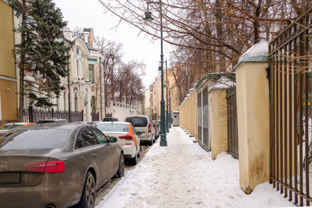 Moscow. Russia. February 25, 2023. Cars are parked along a snow-covered sidewalk in the historic city center on a cloudy winter day.のeditorial素材