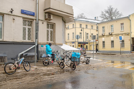 Moscow. Russia. February 25, 2023. A Yandex Food courier with blue thermal bags among several bicycles in Barykovsky Lane in Moscow.のeditorial素材