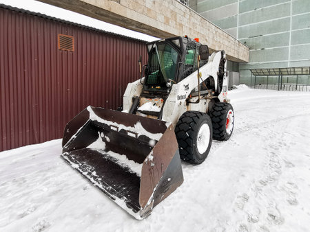 Moscow. Russia. March 6, 2023. A small snow plow Bobcat backhoe loader with a snow shovel. Snowflakes fly in the air.のeditorial素材