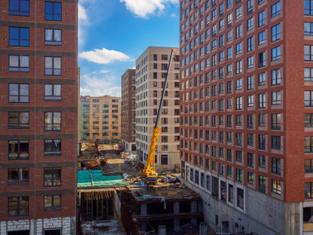 Heavy yellow truck crane is working on a construction site between new modern high-rise buildings. Development, construction equipment truck, construction crane.の写真素材