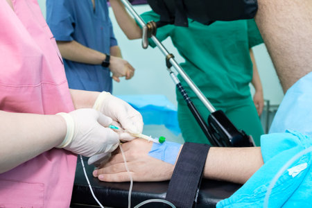 The doctor inserts a catheter into a vein in the patient's wrist to administer drugs during surgery. The doctor's hands in sterile gloves insert the needle into the patient's arm.の写真素材