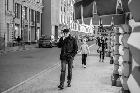 Moscow. Russia. May 20, 2023. A man walks down Vetoshny Lane in Moscow past the windows of the Main Department Store. The man is smoking. Lifestyle photo. Black and white photo.のeditorial素材