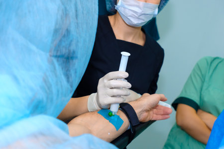 Hands of an anesthesiologist injecting medicine intravenously into the patient's arm using a syringe. Injecting anesthesia through a catheter on a man's arm on the operating table.の写真素材